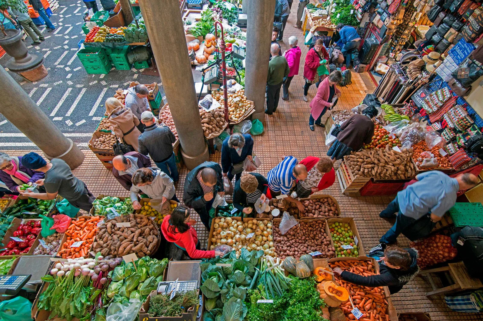 Clientes y clientas en mercado local seleccionando frutas y verduras frescas de productores de proximidad