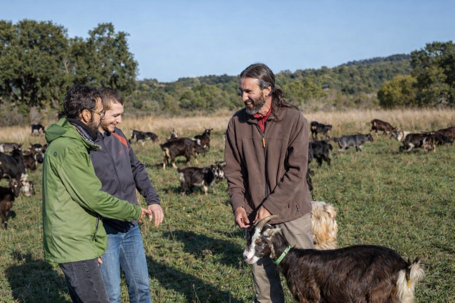 Tres personas conversan en un pasto con cabras en un espacio test agrario de ganadería